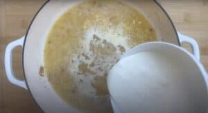 Cream being poured into a pot of simmering broth, combining ingredients for a savory soup or sauce recipe.
